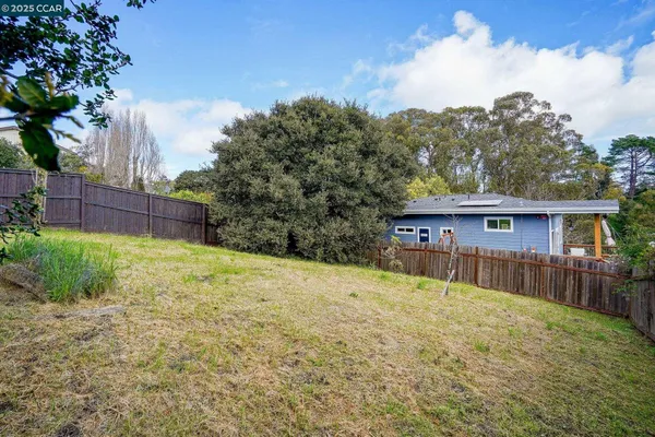 a view of a house with wooden fence and large trees