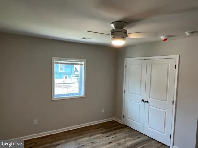 a view of an empty room with wooden floor ceiling fan