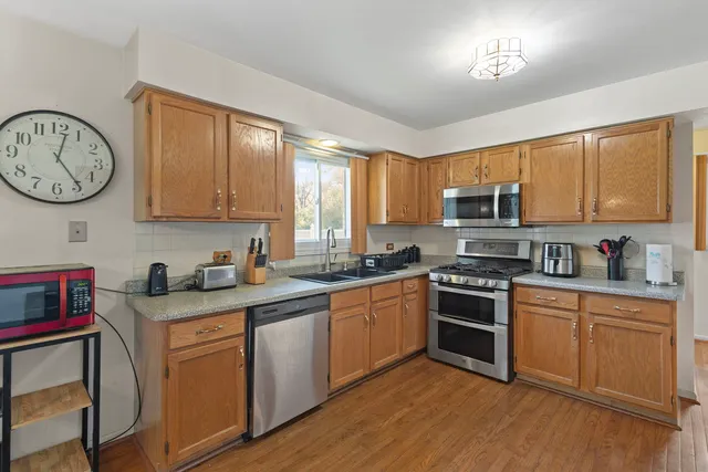 a kitchen with stainless steel appliances granite countertop a stove top oven a sink dishwasher and white cabinets with wooden floor