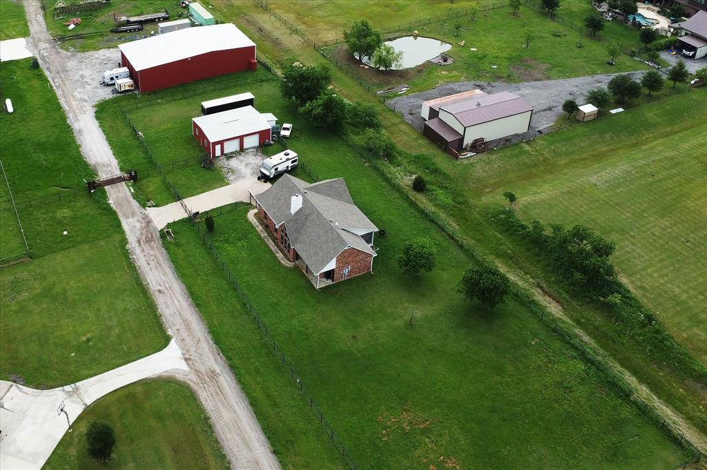 Expansive property featuring a brick residence with a covered front porch, a large red outbuilding, and a secondary red outbuilding with garage doors