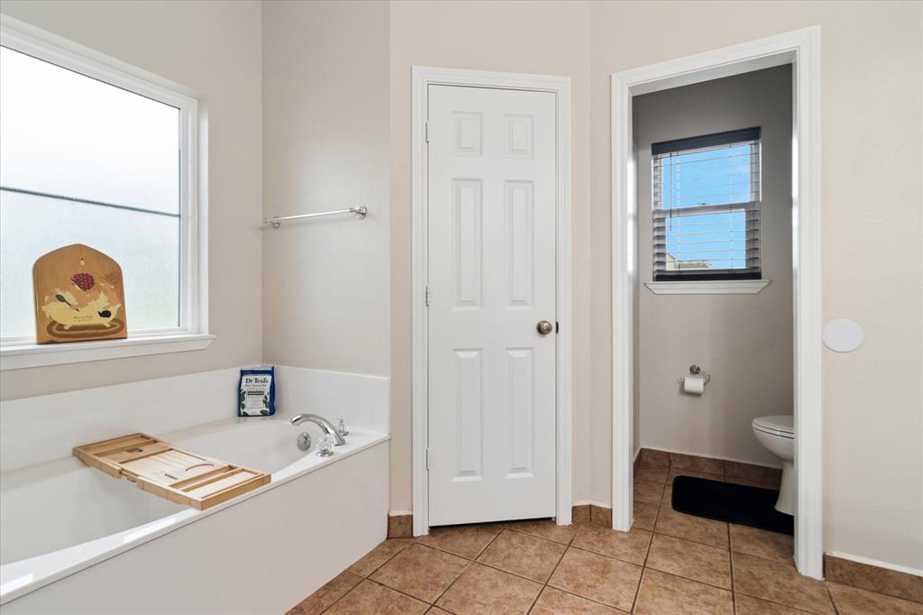 6005 Hawkeye Road Krum, TX 76249 - Photo 18 of 27 Soaking tub with chrome fixtures, frosted glass window, and tile flooring