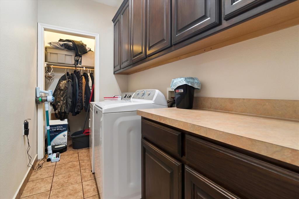 6005 Hawkeye Road Krum, TX 76249 - Photo 21 of 27 Laundry area featuring wood-finish cabinetry, a light-toned countertop, and tile flooring