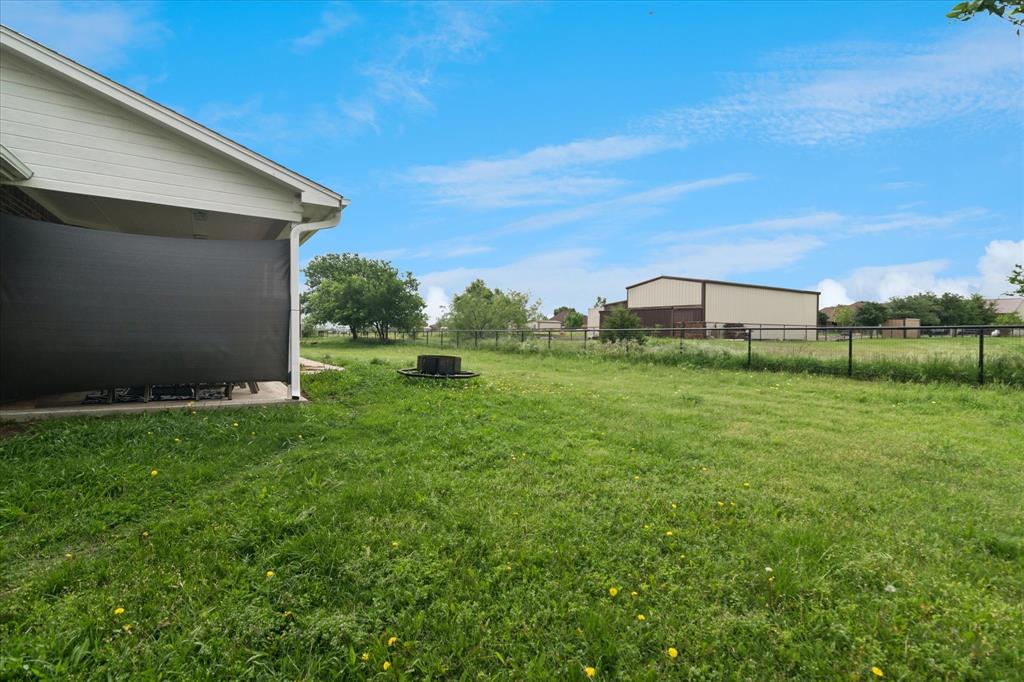 6005 Hawkeye Road Krum, TX 76249 - Photo 25 of 27 Expansive grassy area featuring a black metal fence, mature trees, and a visible outbuilding