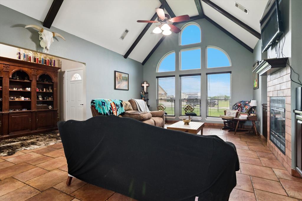 6005 Hawkeye Road Krum, TX 76249 - Photo 10 of 27 Living area featuring vaulted ceilings with exposed wood beams, a ceiling fan, and large arched windows with horizontal blinds