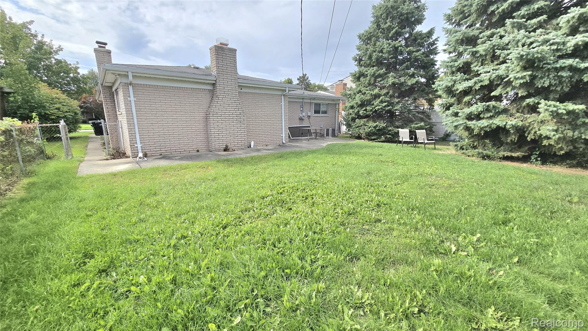 34294 Greentrees Road Sterling Heights, MI 48312 - Photo 19 of 20 Expansive outdoor space featuring a grass lawn, mature evergreen trees, and a brick exterior structure with a prominent chimney