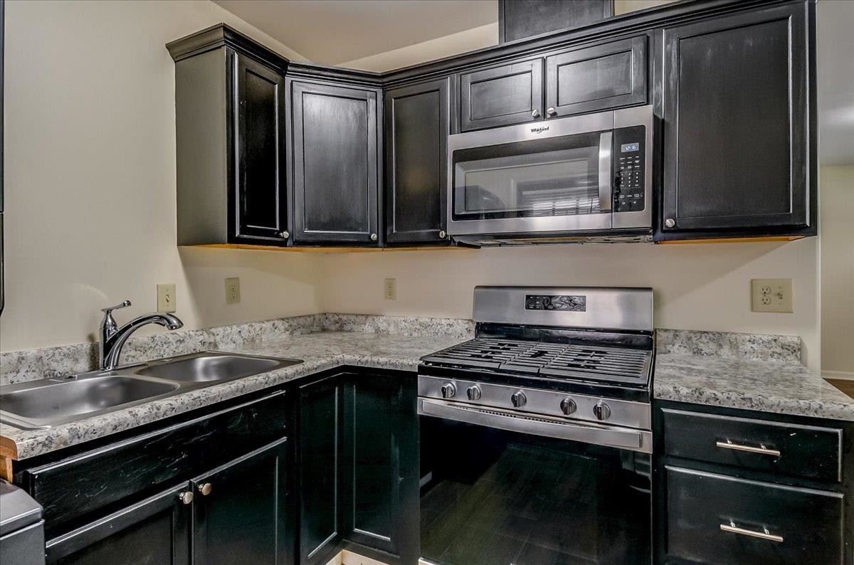 1411 Roberts Road Memphis, TN 38106 - Photo 11 of 24 Kitchen featuring dark cabinetry with crown molding, stainless steel appliances including a gas range and microwave, dual basin stainless steel sink, and speckled countertops