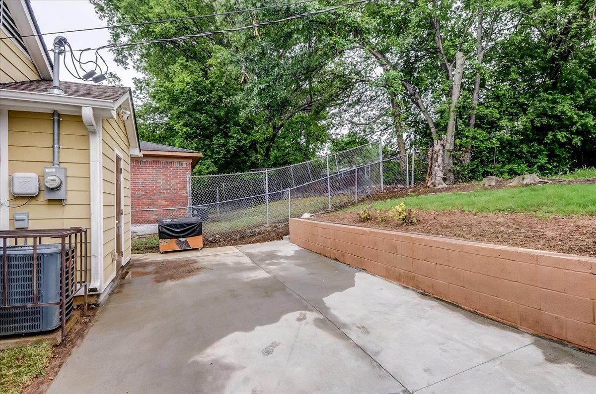 1411 Roberts Road Memphis, TN 38106 - Photo 21 of 24 Concrete patio and walkway with a retaining wall, chain-link fencing, and mature trees