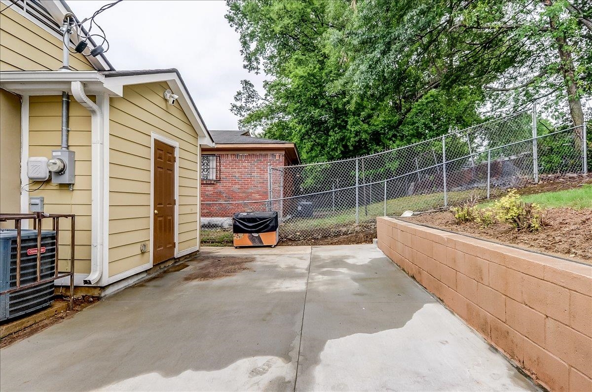 1411 Roberts Road Memphis, TN 38106 - Photo 22 of 24 Concrete patio area featuring a retaining wall, chain-link fencing, and mature trees