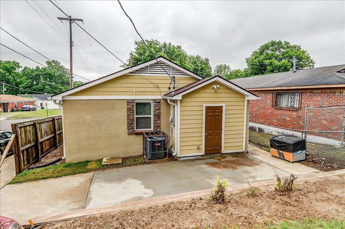 1411 Roberts Road Memphis, TN 38106 - Photo 23 of 24 Rear exterior featuring a detached storage shed with a brown door, smooth stucco siding, horizontal yellow siding, and a stone-accented window frame