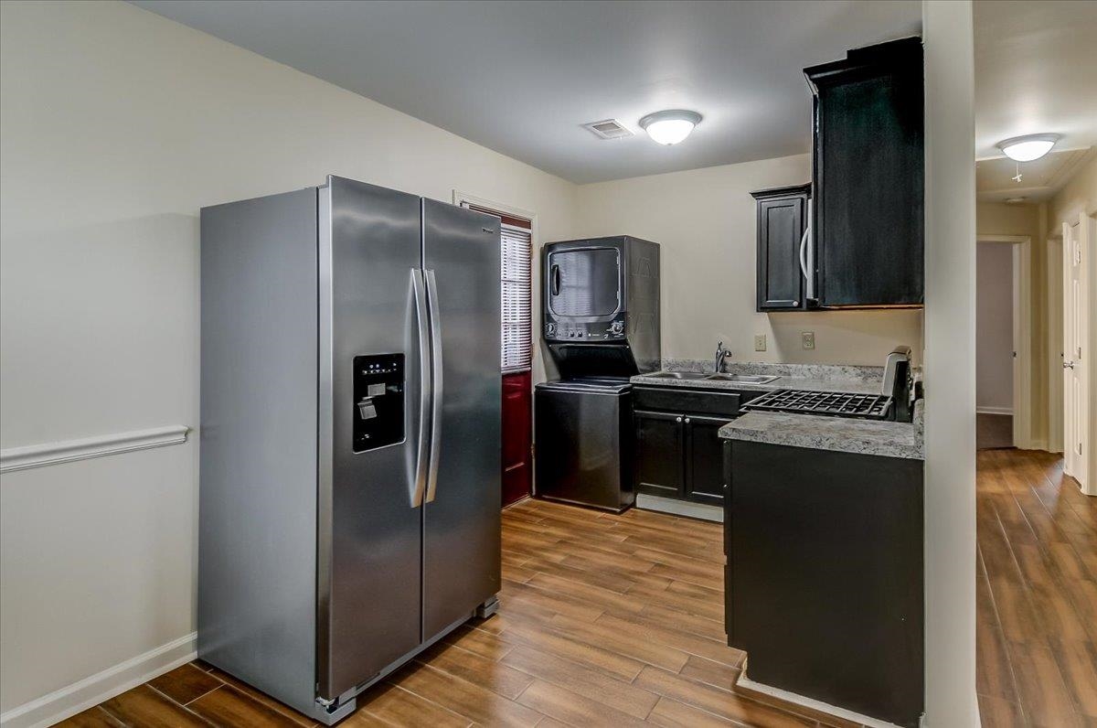 1411 Roberts Road Memphis, TN 38106 - Photo 9 of 24 Stainless steel side-by-side refrigerator, dark wood-finish flooring, black cabinetry, stacked washer and dryer unit, and stone-finish countertops