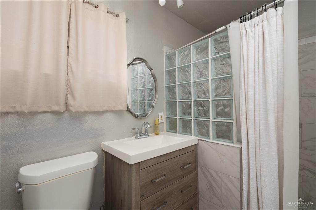 411 East 4th Street Rio Grande City, TX 78582 - Photo 10 of 12 Bathroom featuring a wood-finish vanity with an integrated sink, an ornate wall mirror, and a glass block shower wall