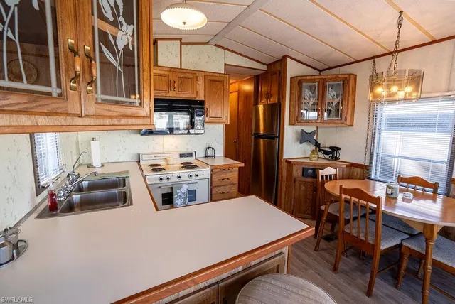 a kitchen with stainless steel appliances granite countertop a refrigerator a sink dishwasher a dining table and chairs with wooden floor