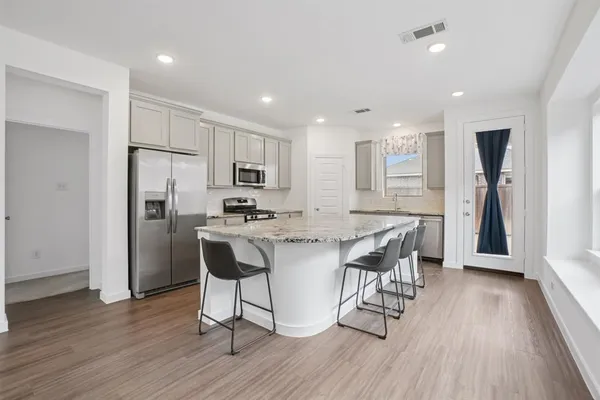 a kitchen with stainless steel appliances kitchen island granite countertop a refrigerator a stove a sink a dining table and chairs with wooden floor