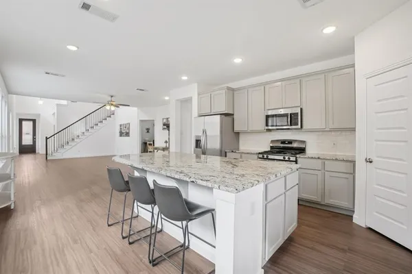 a kitchen with stainless steel appliances kitchen island granite countertop a stove a sink a refrigerator and white cabinets with wooden floor