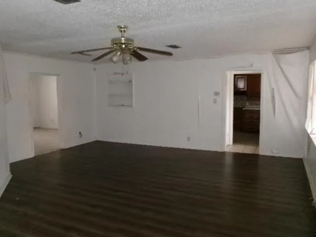 an empty room with wooden floor chandelier fan and windows