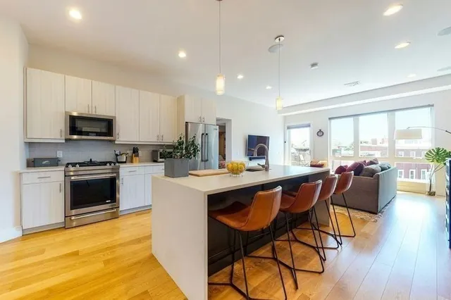 a kitchen with stainless steel appliances kitchen island granite countertop a stove a sink a microwave a dining table and chairs with wooden floor