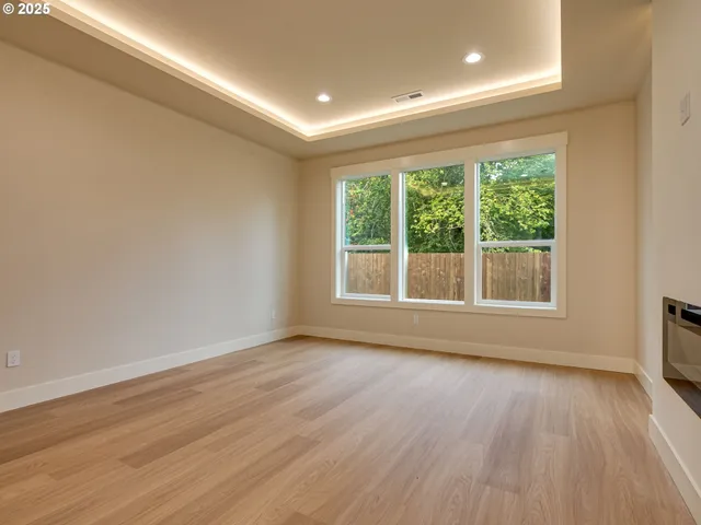 a view of an empty room with wooden floor and a kitchen