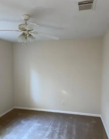 an empty room with a chandelier fan and windows