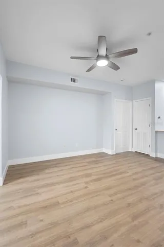 a view of an empty room with wooden floor ceiling fan