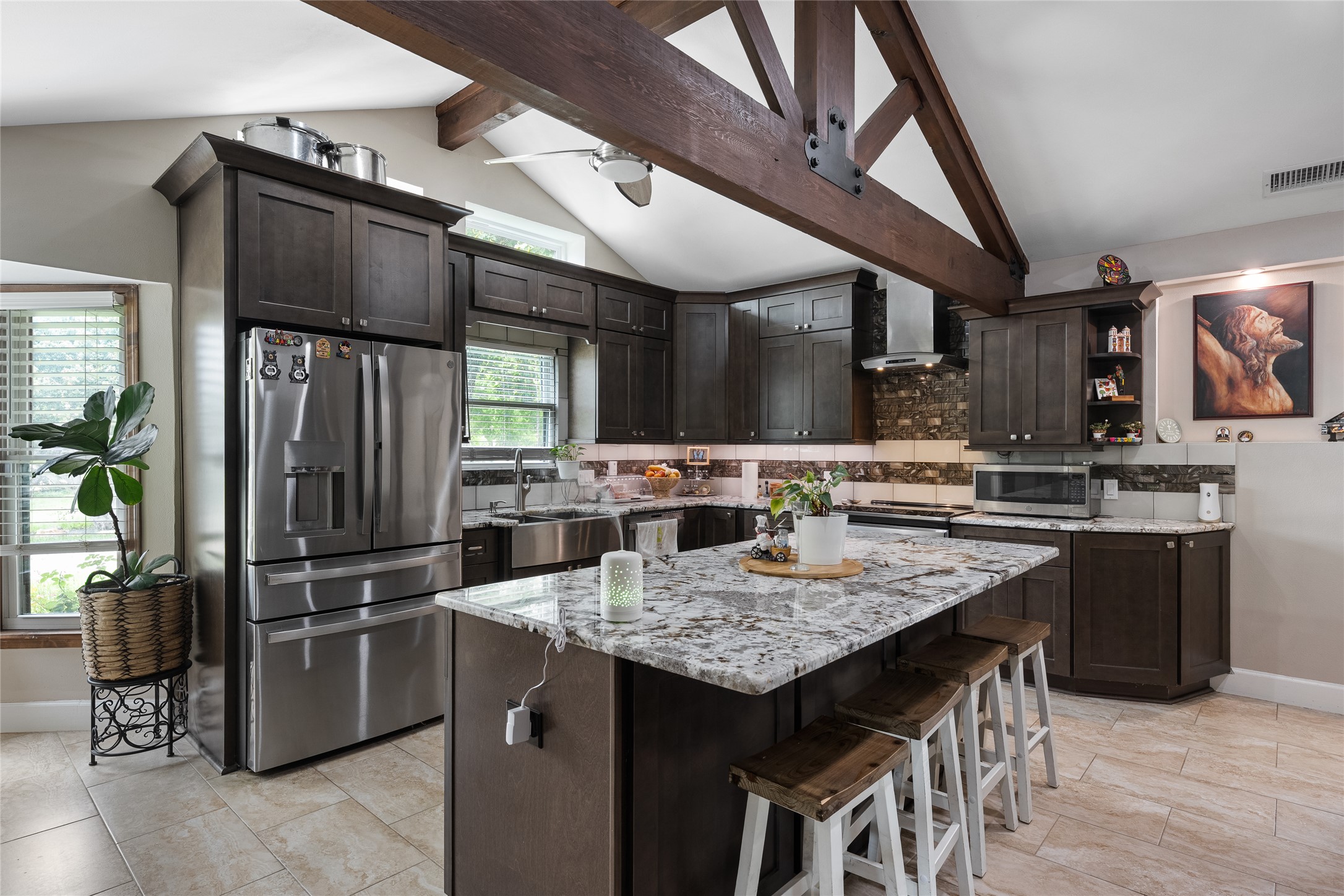 301 Oak Ridge Road Georgetown, TX 78628 - Photo 5 of 34 Kitchen featuring an expansive island with a light-toned countertop, dark wood-finish cabinetry, stainless steel appliances, a deep basin sink, and exposed ceiling beams
