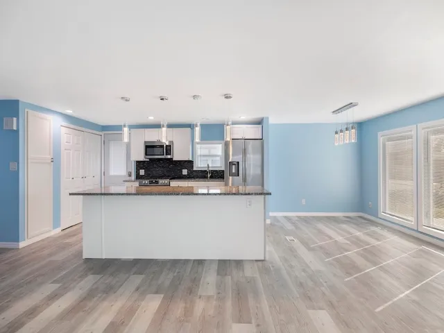 a large kitchen with granite countertop a refrigerator a sink a stove a microwave and wooden floor