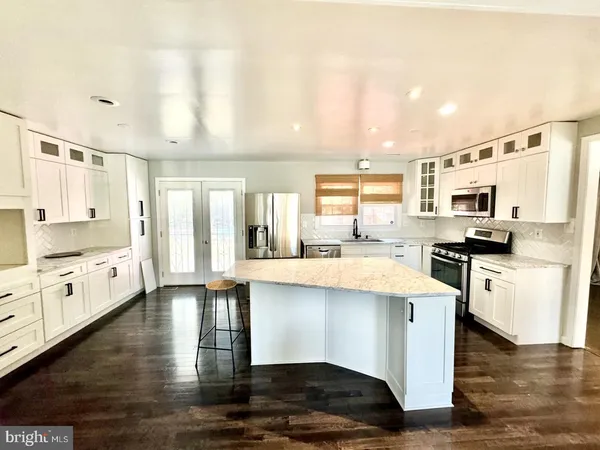 a kitchen with stainless steel appliances kitchen island granite countertop a stove top oven a sink a refrigerator white cabinets and wooden floor