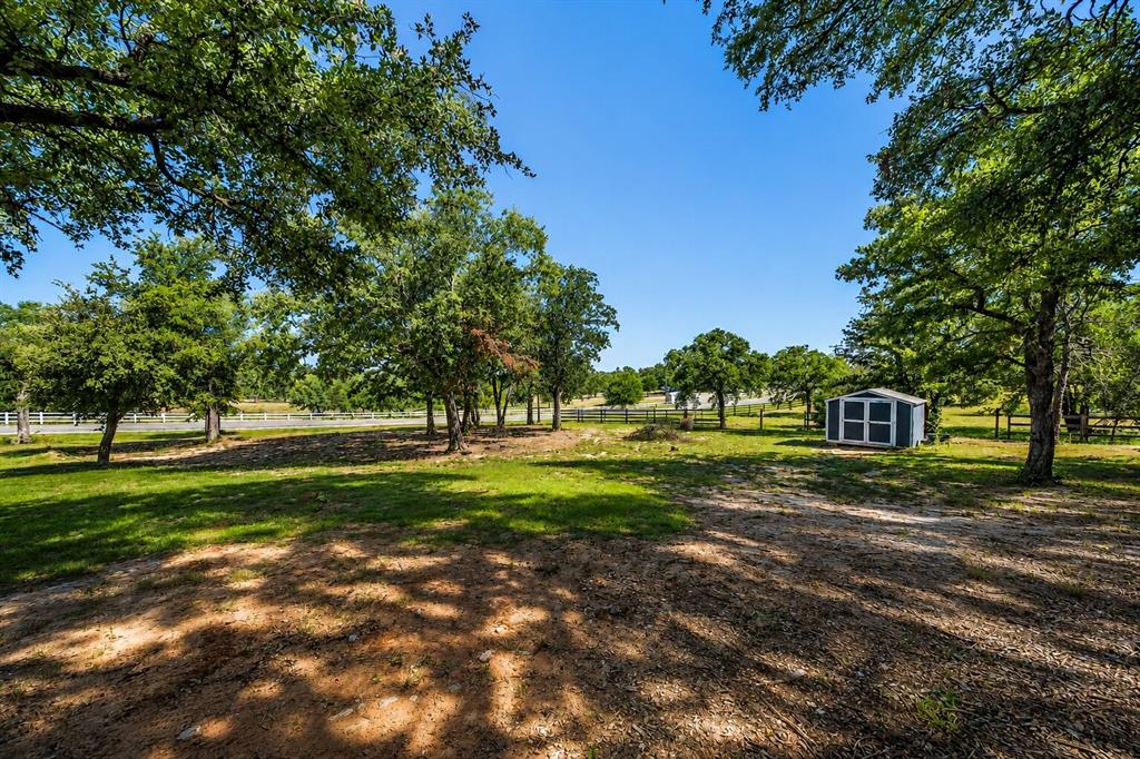 117 Rock Salt Drive Springtown, TX 76082 - Photo 36 of 38 Expansive outdoor space featuring a detached storage shed with a white trim, mature deciduous trees, and a grassy lawn