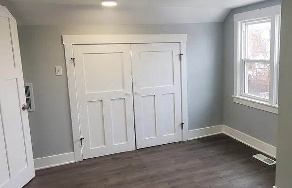 an empty room with wooden floor closet and windows