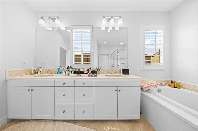 a bathroom with a double vanity sink a mirror a bathtub and next to a window