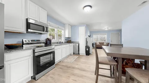 a kitchen with stainless steel appliances granite countertop a stove a sink a microwave a dining table and chairs with white cabinets
