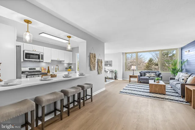 a living room with stainless steel appliances a dining table wooden floor and a large window