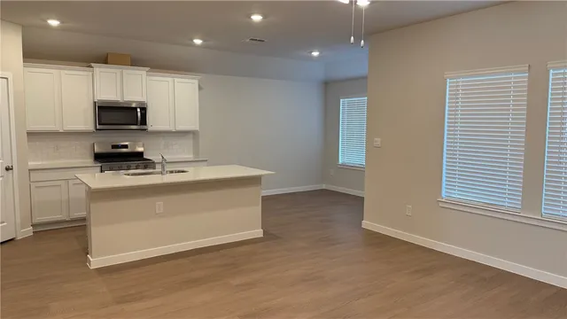 a room with kitchen island stainless steel appliances a sink a stove a microwave a sink and cabinets