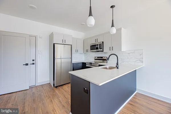 a kitchen with stainless steel appliances a sink a stove a refrigerator a center island with wooden floor and cabinets