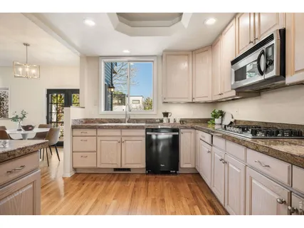 a kitchen with stainless steel appliances granite countertop a stove a sink dishwasher and white cabinets with wooden floor