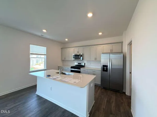 a kitchen with stainless steel appliances granite countertop a refrigerator a sink dishwasher a stove and white countertops with wooden floor