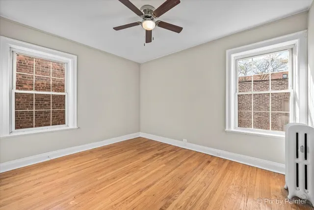 an empty room with wooden floor fan and windows