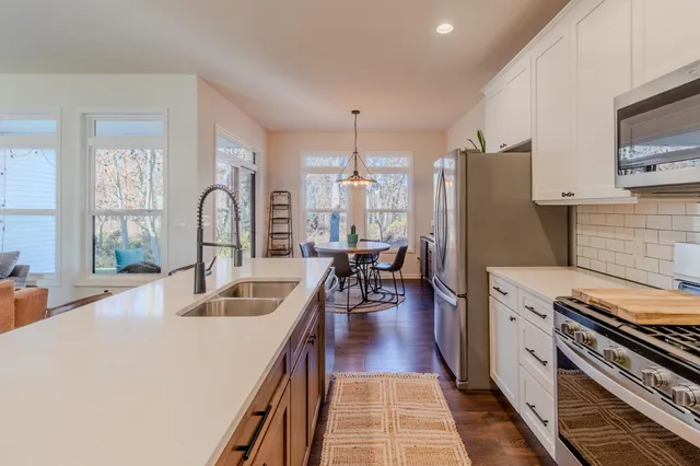 a kitchen with stainless steel appliances a stove a sink dishwasher a refrigerator white cabinets and wooden floor