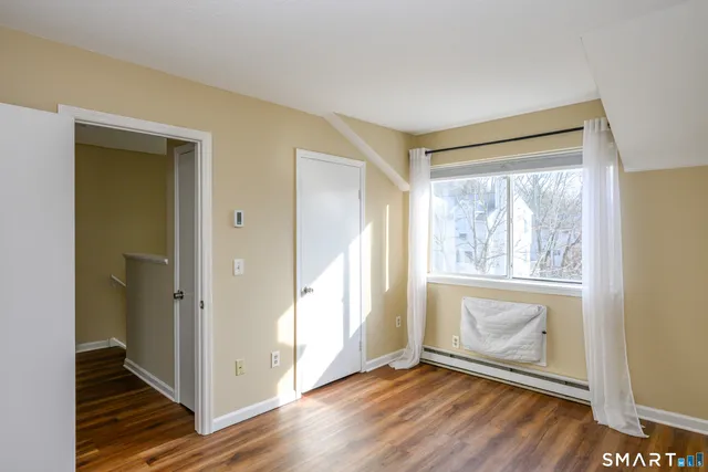 a view of an empty room with wooden floor and a window