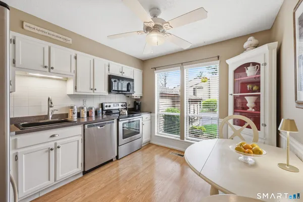 a kitchen with stainless steel appliances granite countertop a stove a sink a refrigerator and white cabinets with wooden floor