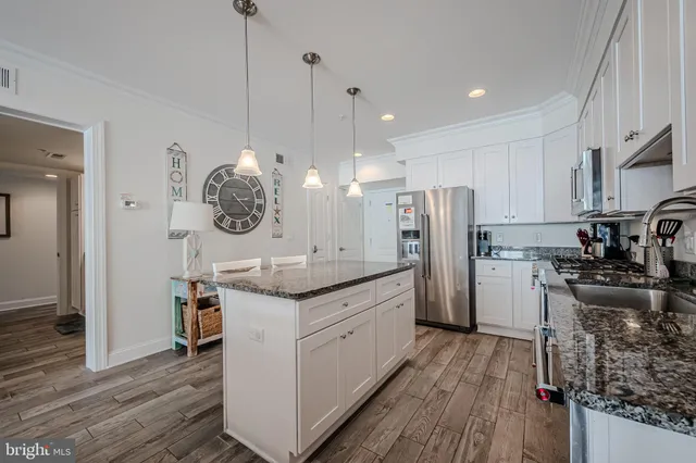 a kitchen with stainless steel appliances granite countertop a refrigerator a oven a sink and white cabinets with wooden floor