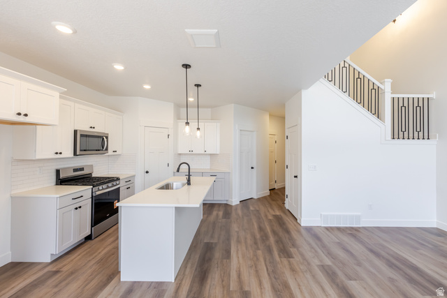 4812 Heartwood Road, Unit 424 Mapleton, UT 84664 - Photo 10 of 20 Kitchen with stainless steel appliances, white cabinets, light wood-style flooring, an island with sink, and decorative backsplash