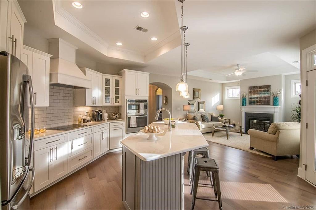 a kitchen with stainless steel appliances granite countertop a refrigerator a sink dishwasher a stove and white cabinets with wooden floor