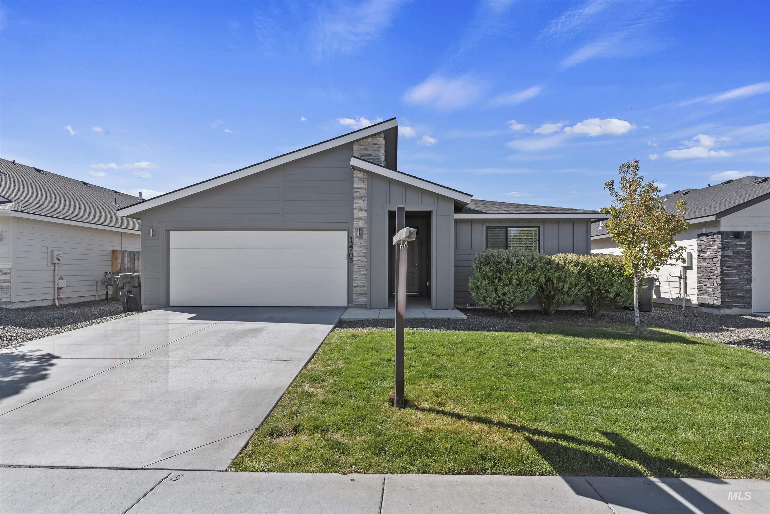 12703 West Fig Street Boise, ID 83713 - Photo 2 of 26 Mid-century home featuring board and batten siding, an attached garage, concrete driveway, a front yard, and stone siding