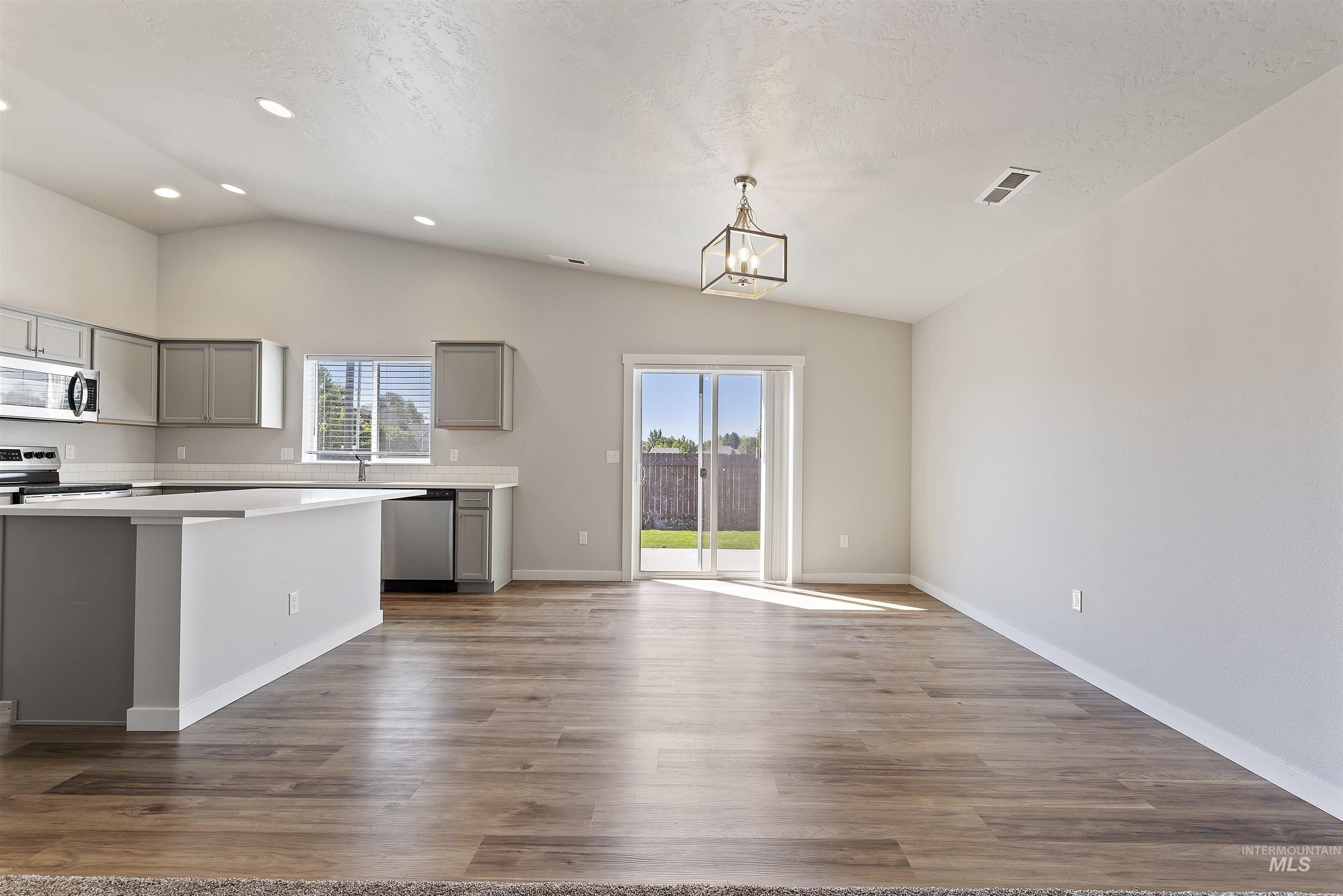 12703 West Fig Street Boise, ID 83713 - Photo 8 of 26 Kitchen featuring gray cabinets, stainless steel appliances, vaulted ceiling, light wood-type flooring, and a chandelier