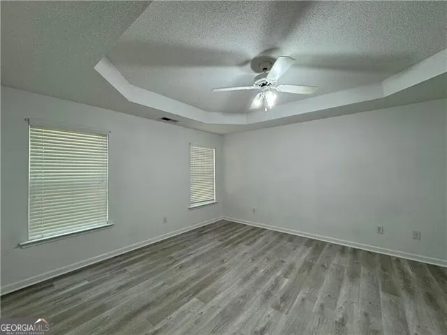 an empty room with wooden floor ceiling fan and windows