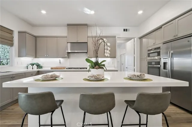 a kitchen with stainless steel appliances kitchen island granite countertop a dining table chairs and a refrigerator