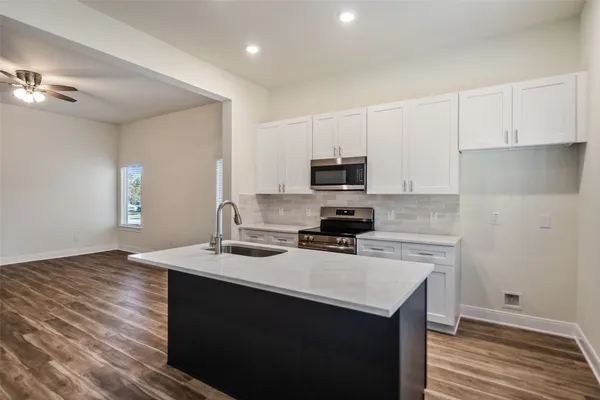 a kitchen with kitchen island a sink dishwasher stove and white cabinets with wooden floor