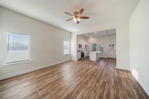 a view of an empty room and a kitchen with wooden floor