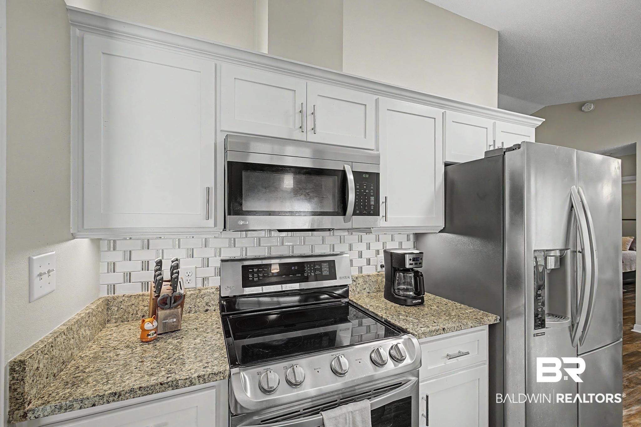 2808 Pine Ridge Drive Lillian, AL 36549 - Photo 16 of 47 Kitchen featuring white shaker-style cabinetry with crown molding, stainless steel appliances, granite countertops, and a subway tile backsplash