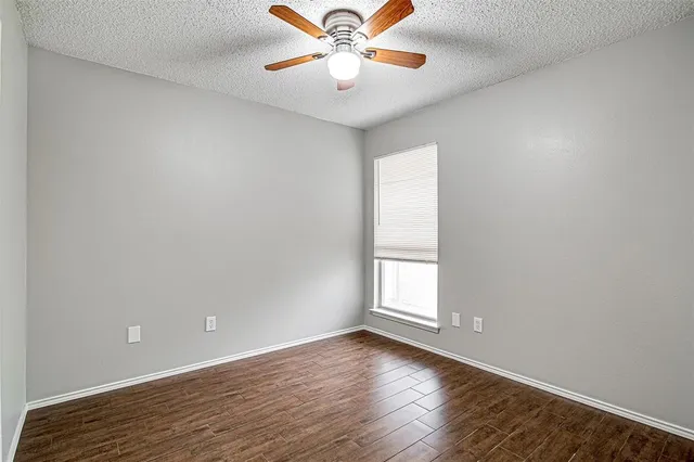 a view of an empty room with wooden floor and a ceiling fan